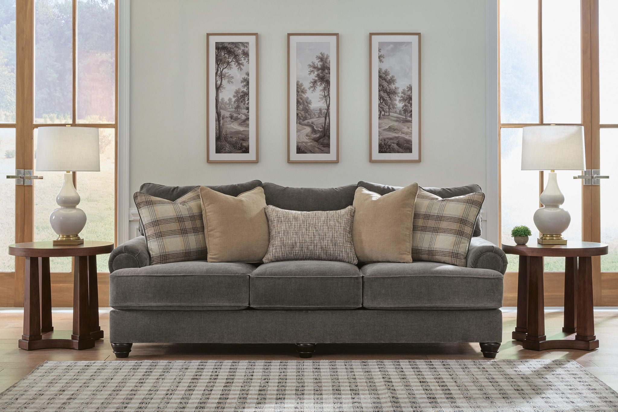 Gray upholstered sofa with tufted arms and plaid and tan throw pillows