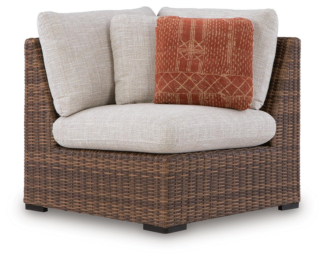 Wicker corner chair with beige cushion and patterned orange throw pillow