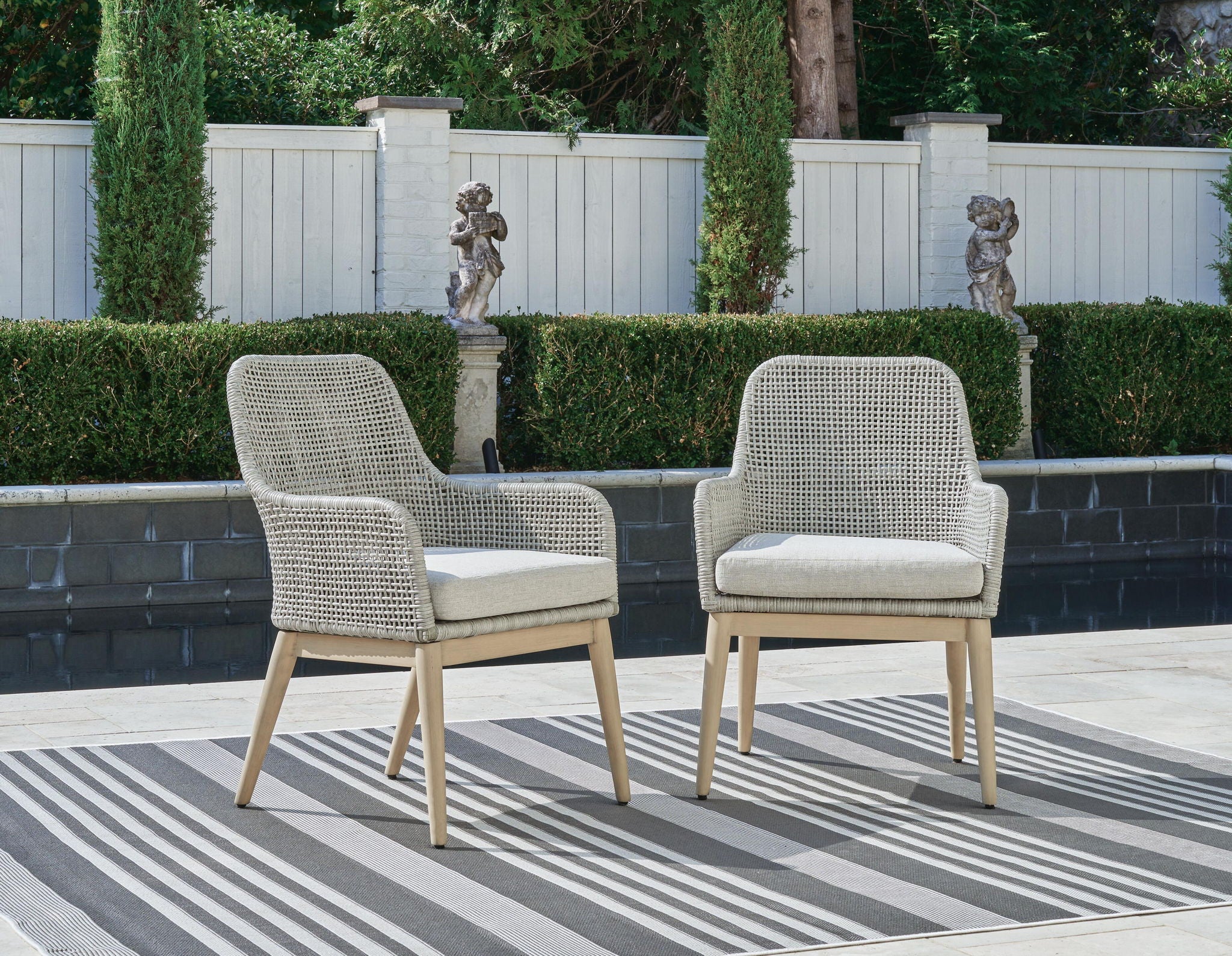 Pair of gray arm chairs with white seat cushions, woven backs, wooden tapered legs.