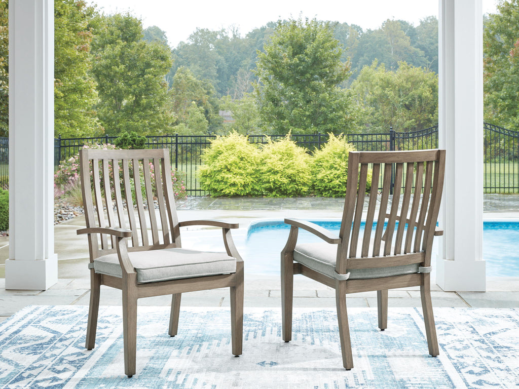 Two wooden arm chairs with slatted backs and beige seat cushions on patio.