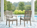 Two wooden arm chairs with slatted backs and beige seat cushions on patio.