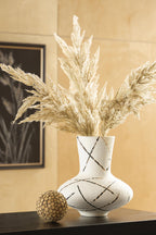 Cream vase holding dried pampas grass, black and brown crisscross line pattern.