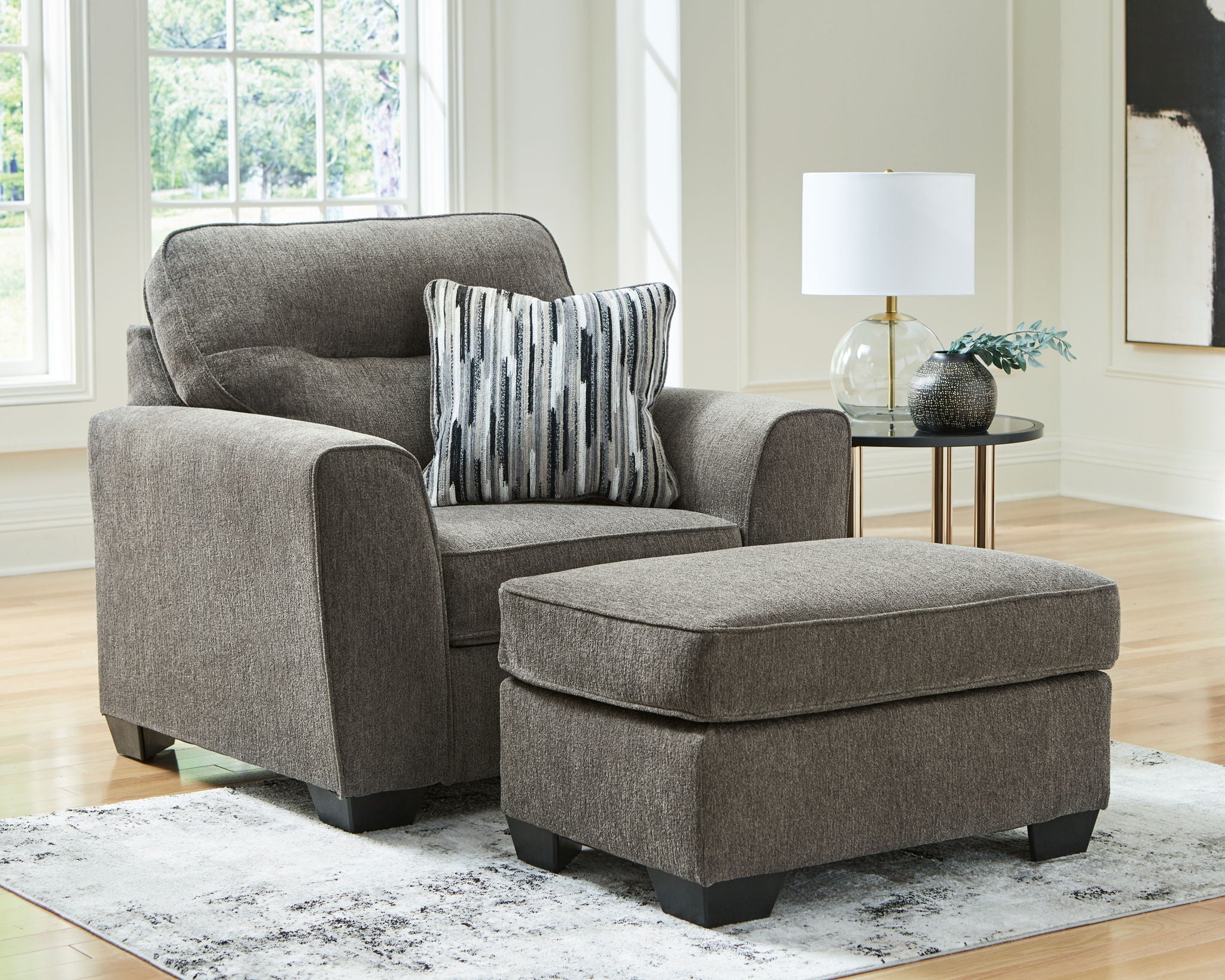 Light brown upholstered armchair with square ottoman and two striped throw pillows