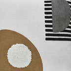 Close-up of white pillow with brown panel, textured white round applique, and striped trim