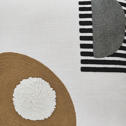 Close-up of white pillow with brown panel, textured white round applique, and striped trim