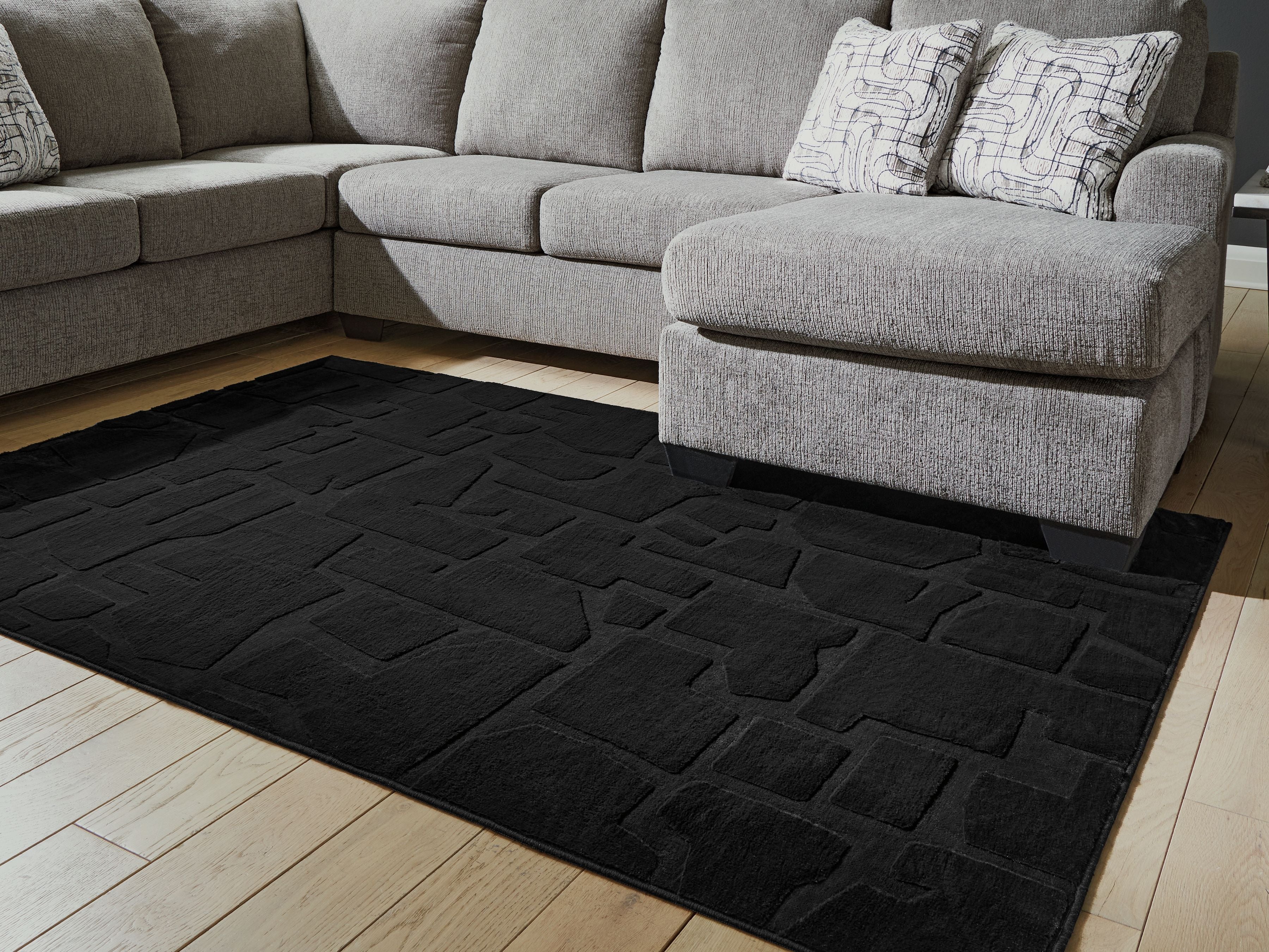 Washable rug, black brick-pattern design on light wood floor, angled view
