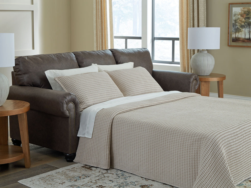 Queen sofa sleeper with pull-out bed and light plaid bedding on dark umber upholstery