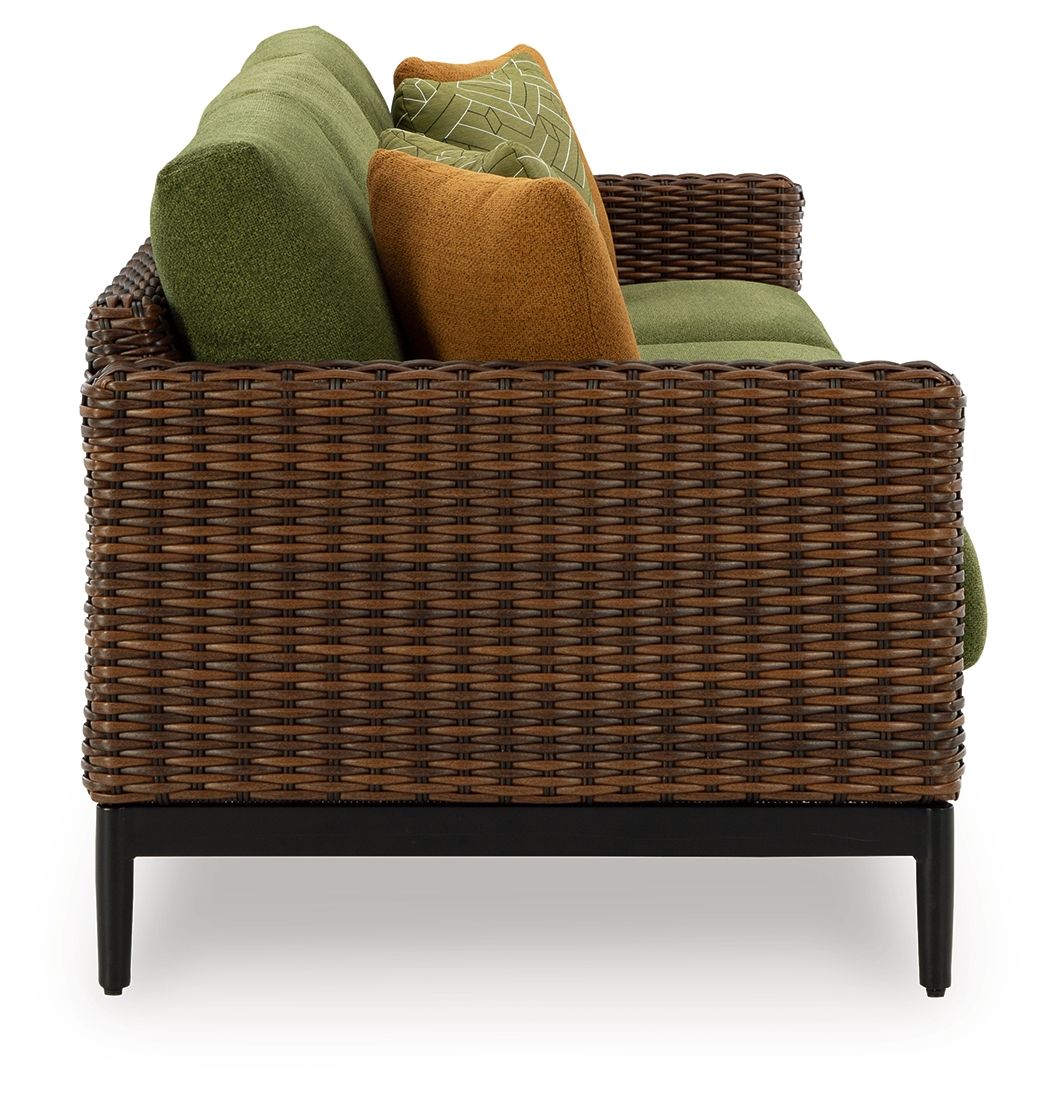 Woven wicker sofa with green cushions, brown accent pillow, and black legs