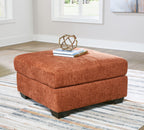 Rust-orange upholstered accent ottoman with cushioned square top and dark block legs.