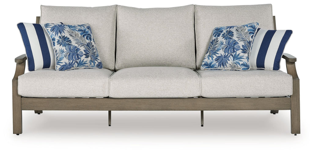 Light gray sofa with three seat cushions and two blue patterned pillows, dark wood legs