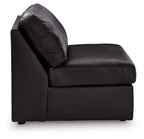 Black armless accent chair with curved back and arm-free sides, leather-look upholstery.