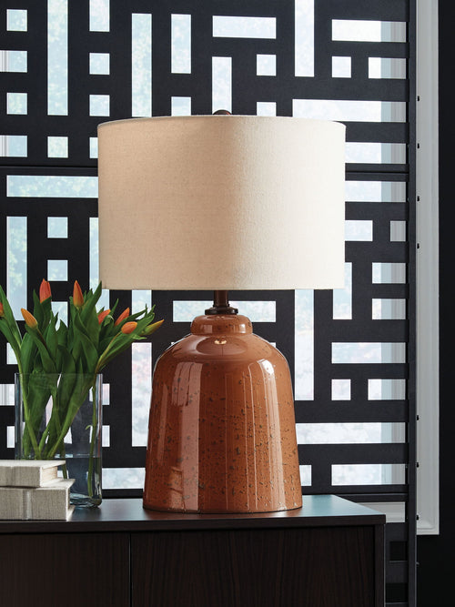 Rust glass table lamp with beige fabric shade, shown on a console