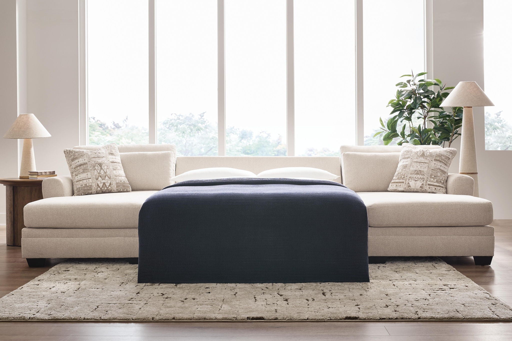 Beige sectional sofa with chaise and patterned pillows, shown with a dark ottoman/cover.