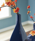 Blue ceramic vase holding red and orange blossoms on dark stems
