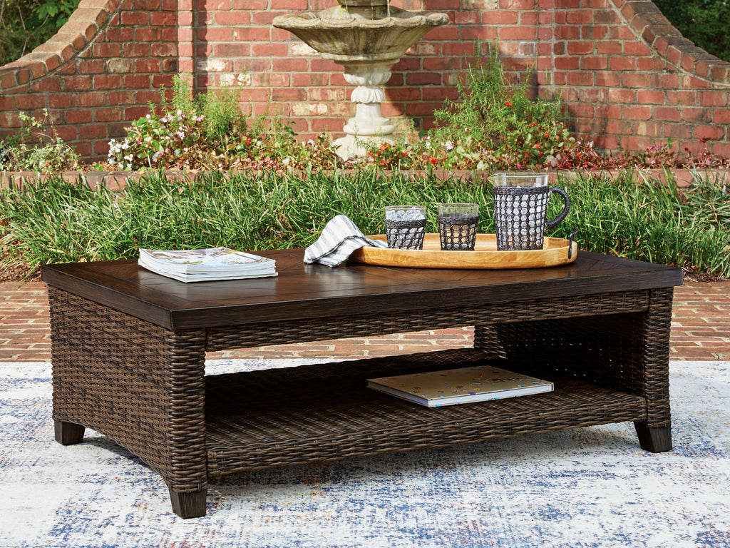 Outdoor rectangular table with dark brown top and woven base, featuring a lower shelf