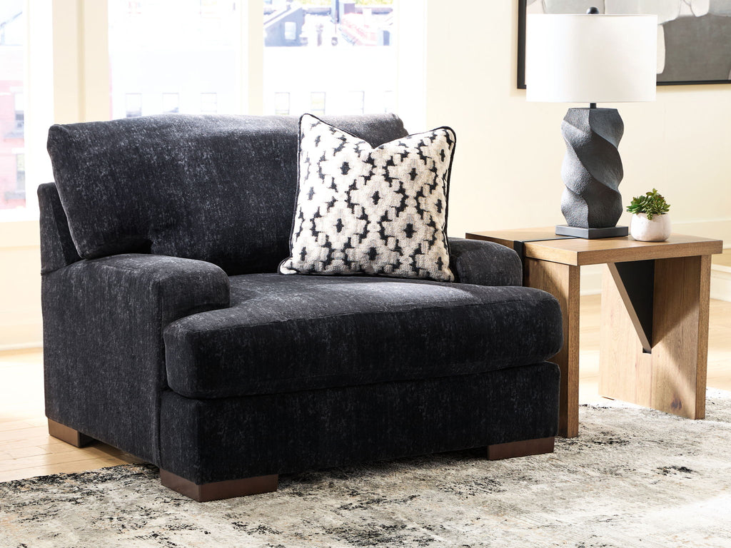 Black chair-and-a-half with open arm profile, thick seat, and monochrome patterned pillow