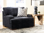 Black chair-and-a-half with open arm profile, thick seat, and monochrome patterned pillow