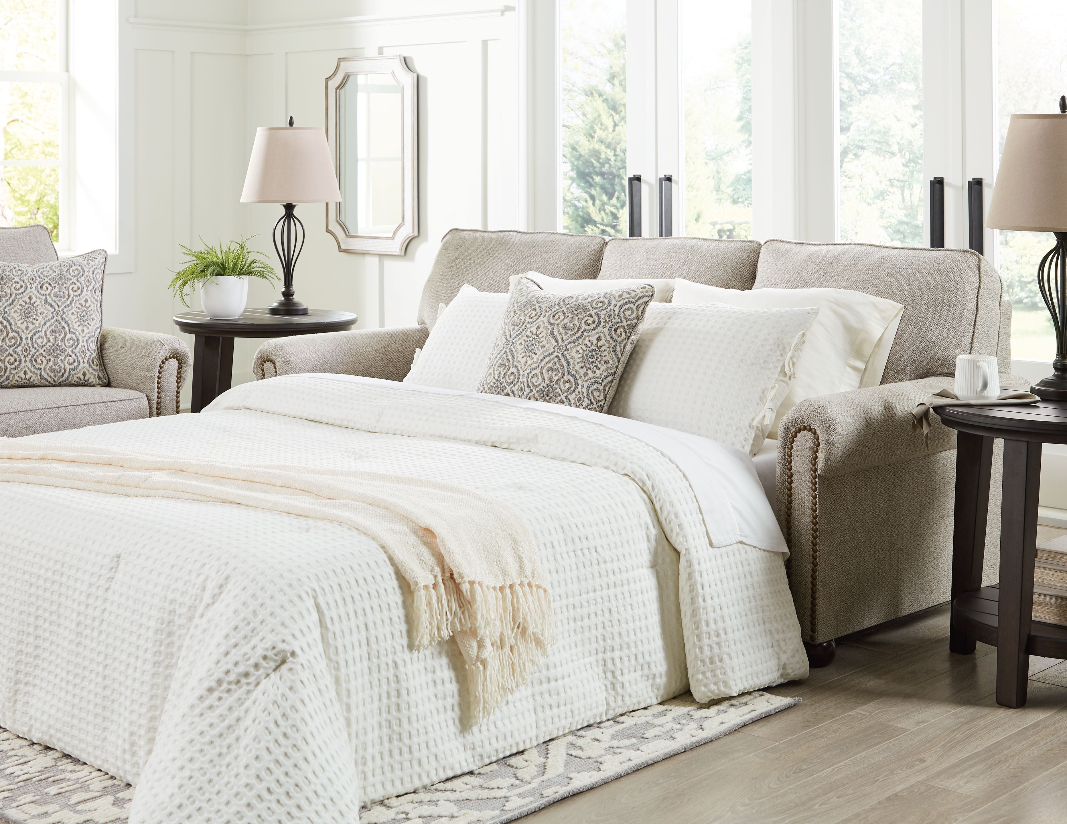 Queen sofa sleeper open for sleeping with white bedding and patterned throw pillows