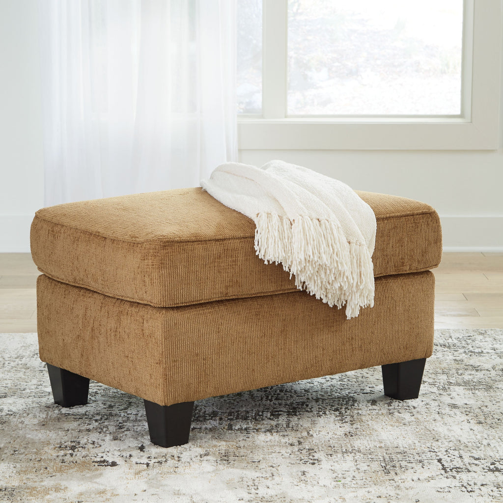 Light brown ottoman with cushioned seat and one corner throw blanket, block legs