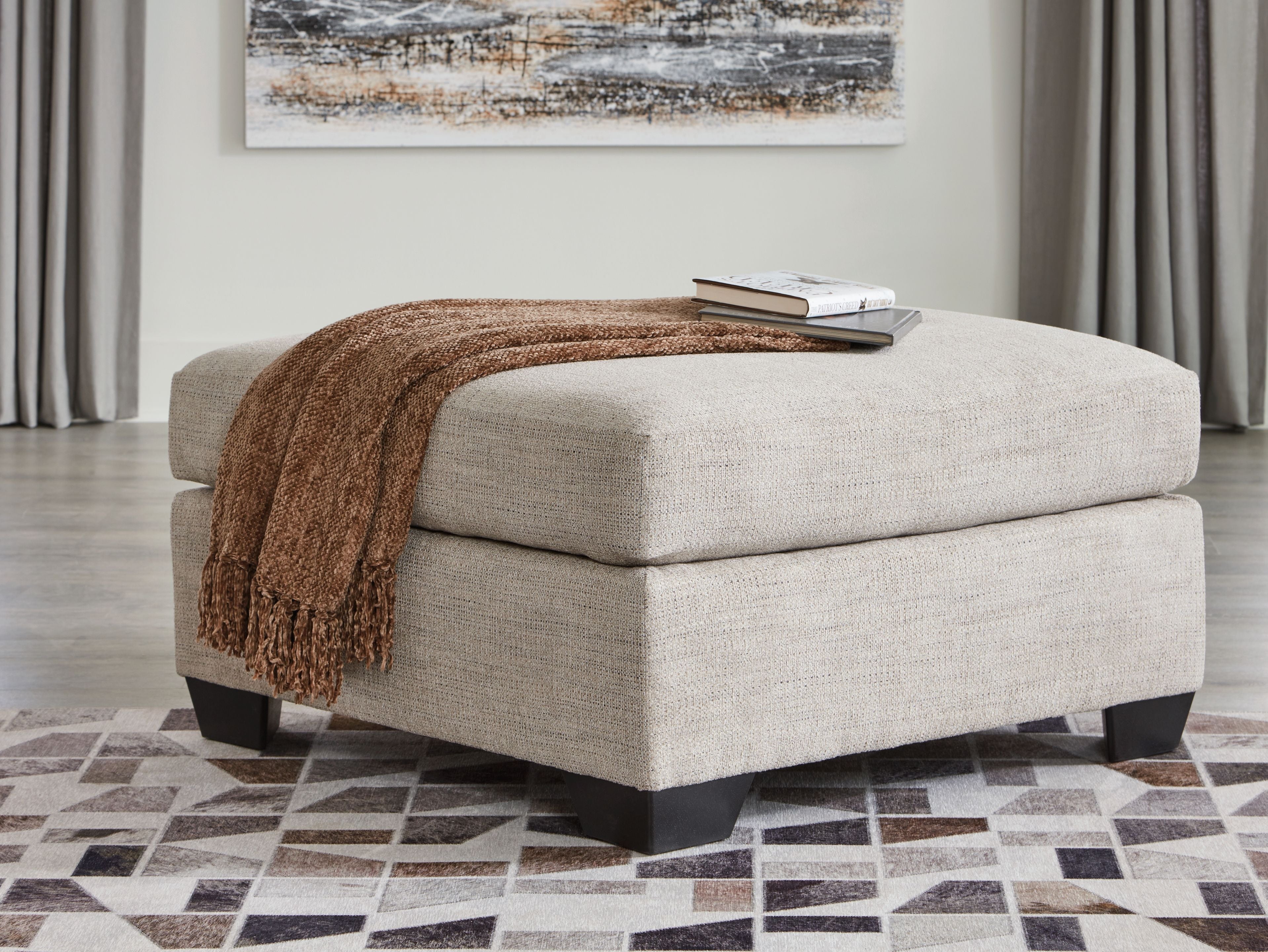 Oversized ottoman with light beige fabric, blocky legs, and a thick cushioned seat.