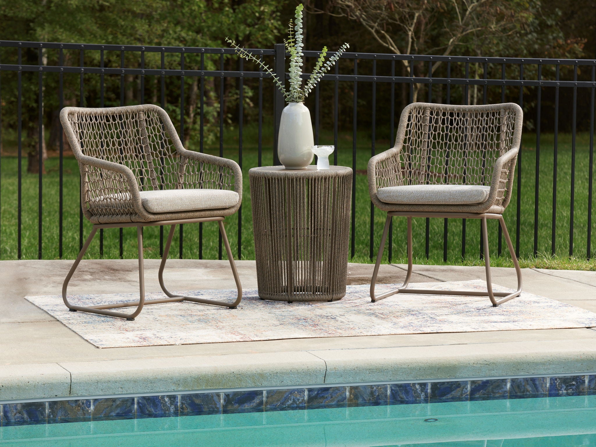 Outdoor patio set with two beige mesh chairs and a round beige side table.