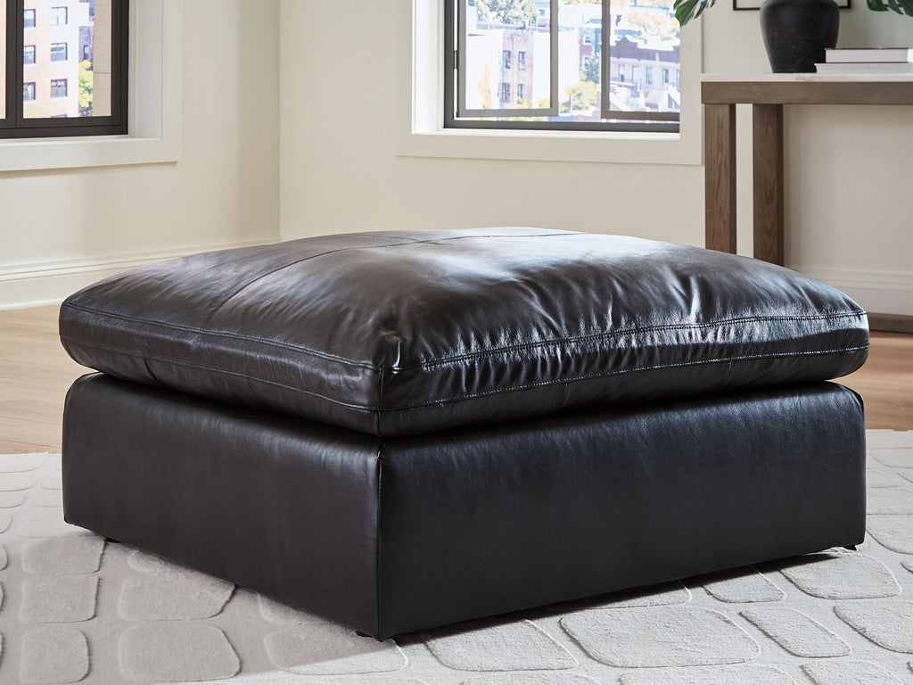 Black oversized accent ottoman with padded seat, rounded top, and low rectangular base