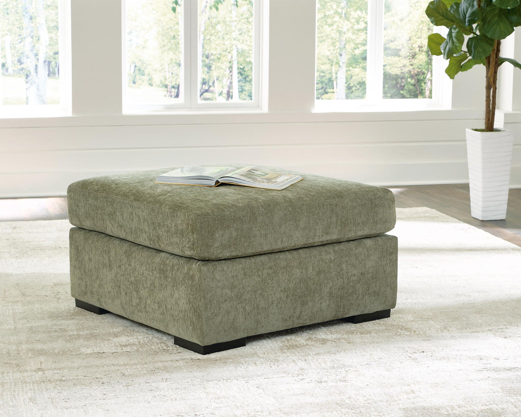 Oversized accent ottoman in green upholstered fabric with square cushioned top and dark legs.