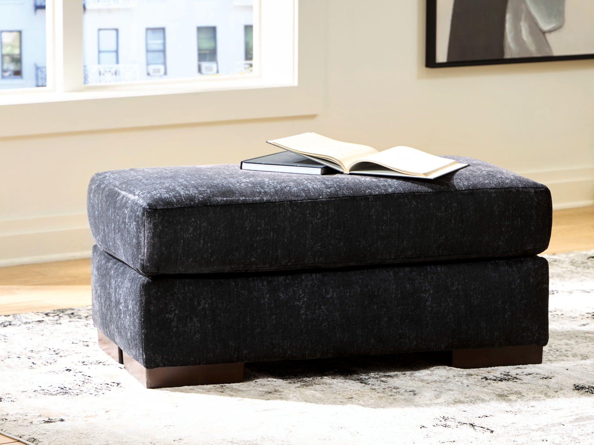 Black fabric ottoman with cushioned lid and dark wooden legs, low rectangular shape