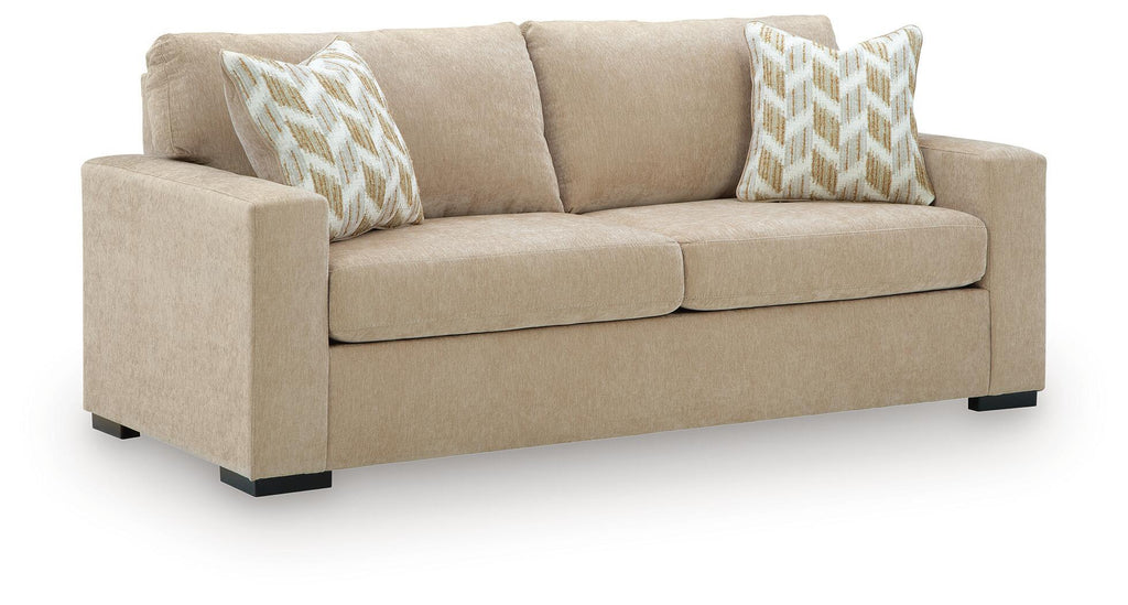 Sofa sleeper in light tan fabric with two patterned throw pillows and black feet