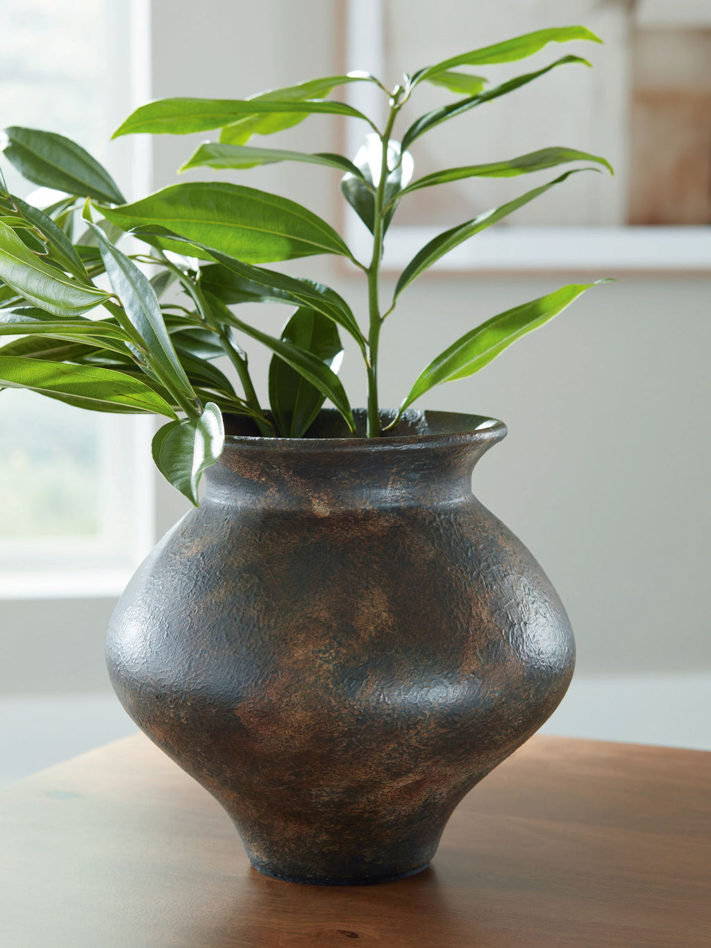 Antique brown vase holding green leafy stems, bulbous shape and flared top