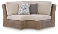 Beige curved corner chair with seat cushion, woven wicker base, zebra accent pillow