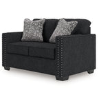 Charcoal loveseat with two patterned pillows and nailhead studded arm panels