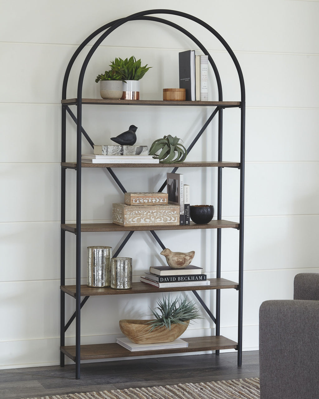 Arched-top black metal bookcase with brown shelves and decorative items on tiers