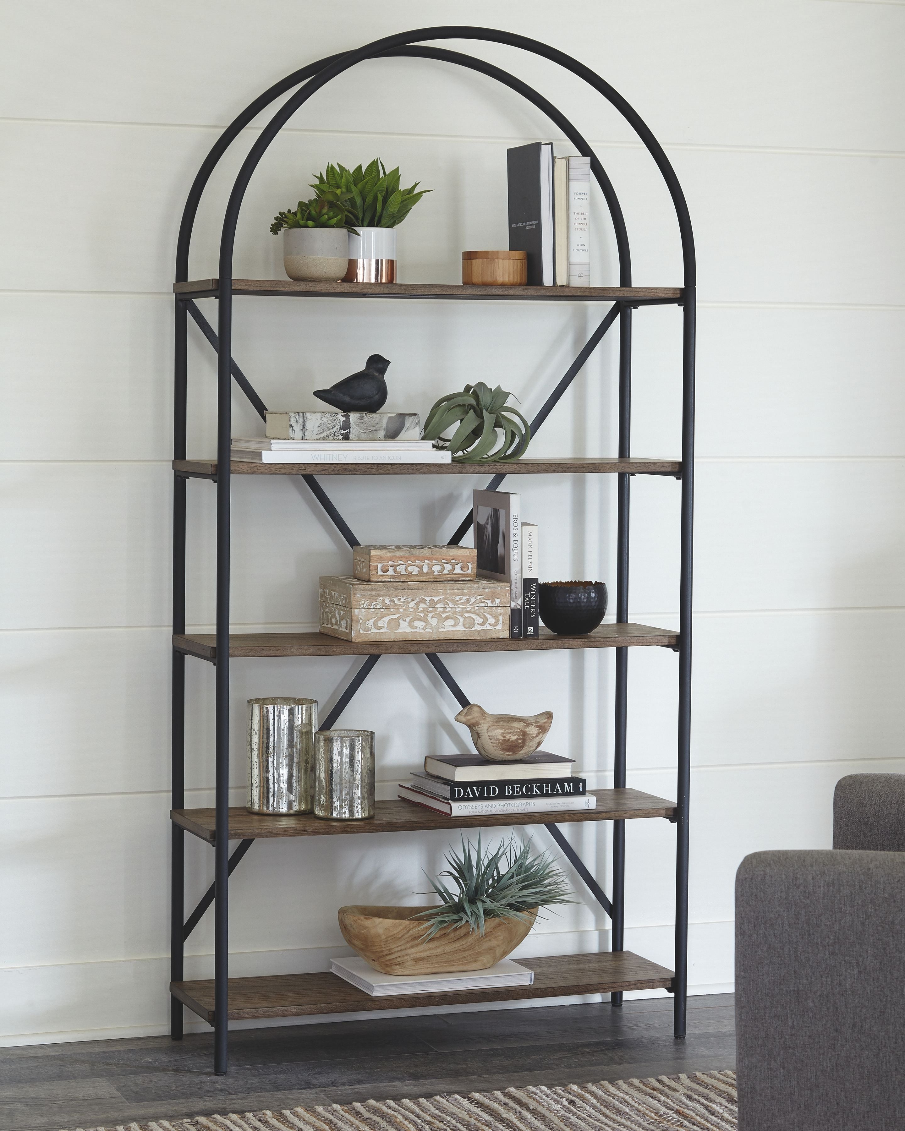 Arched-top black metal bookcase with brown shelves and decorative items on tiers