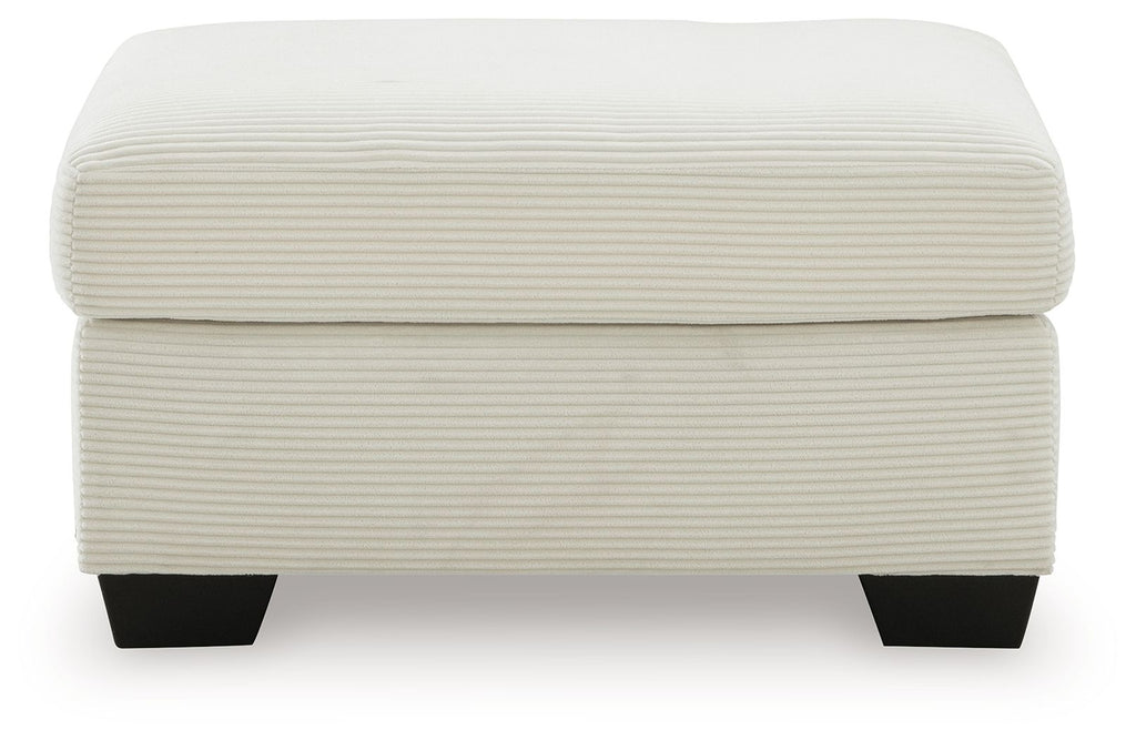 Cream upholstered ottoman with padded lid and ribbed sides, supported by dark legs