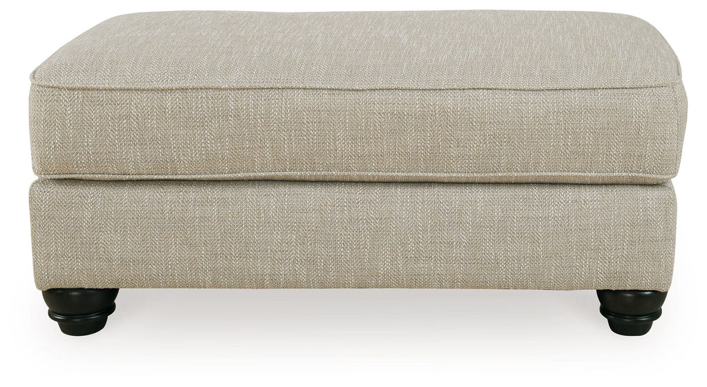 Fog beige ottoman with cushioned top, clean sides, and dark turned legs