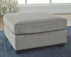 Light gray upholstered accent ottoman with padded seat and short dark legs