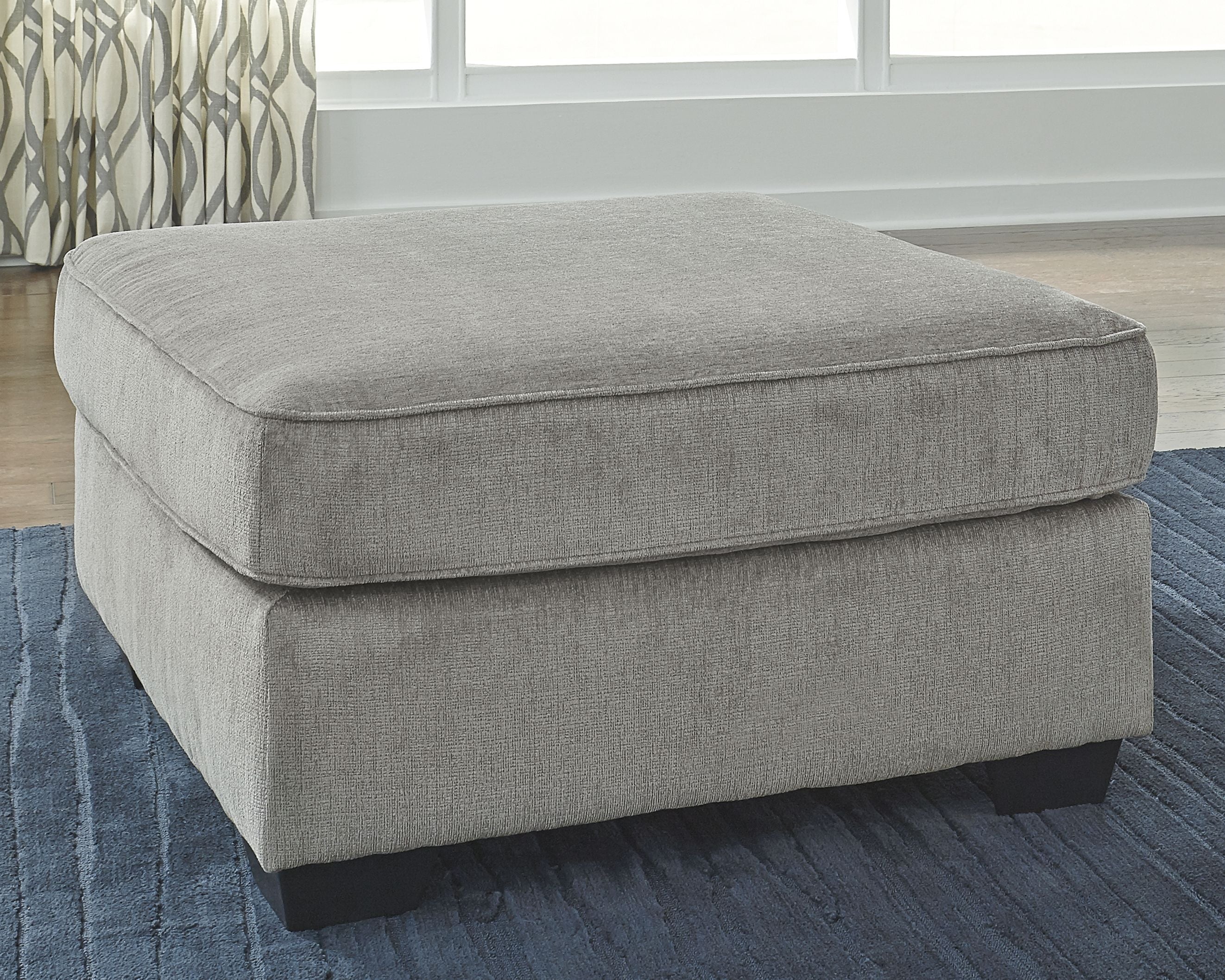 Light gray upholstered accent ottoman with padded seat and short dark legs