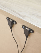 Black dual outlet ports on the side panel of a nightstand, with two cords