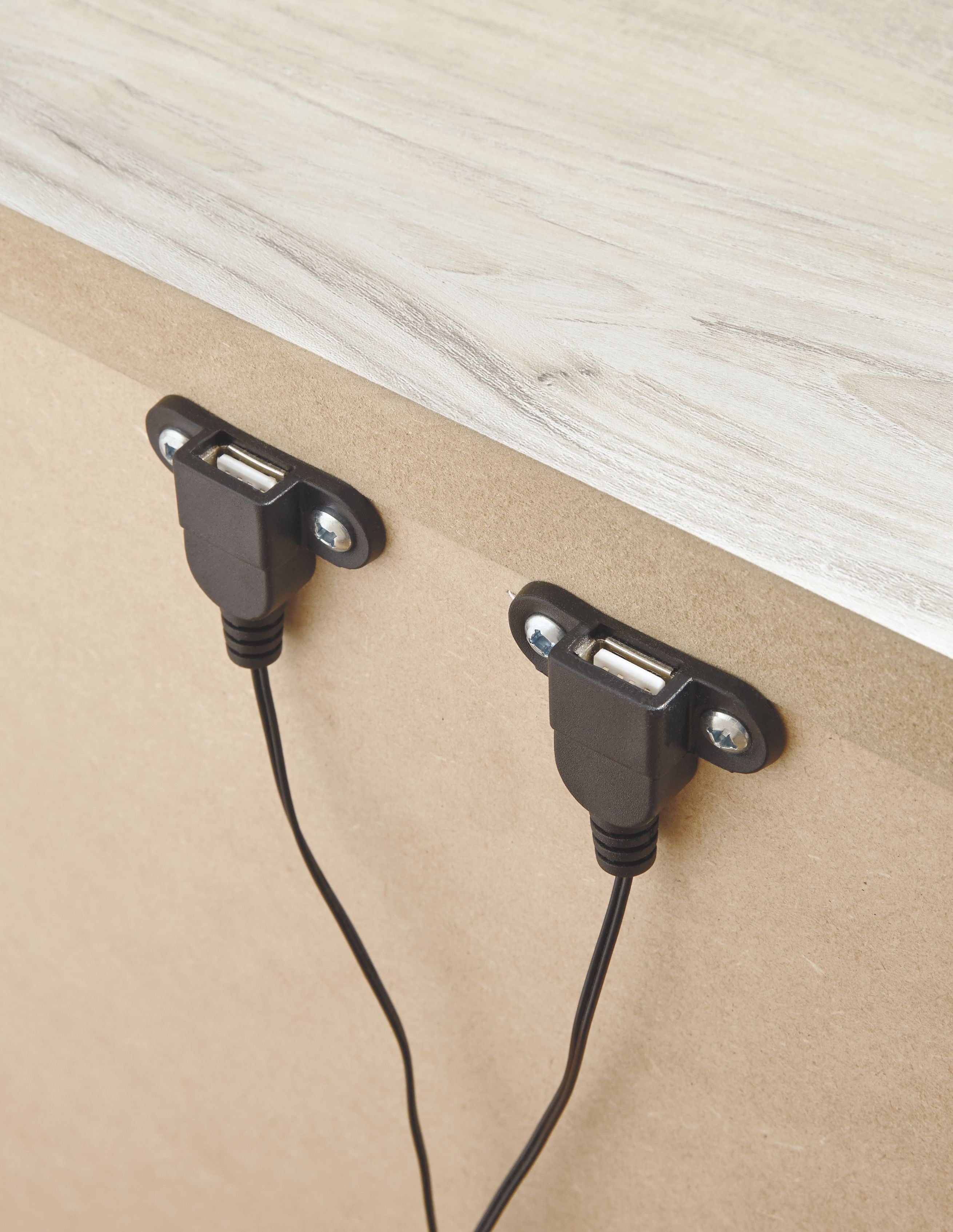 Black dual outlet ports on the side panel of a nightstand, with two cords