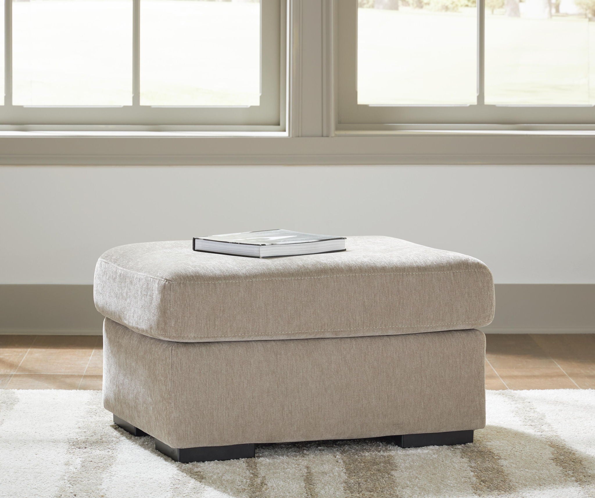 Beige upholstered ottoman with square padded top and black legs
