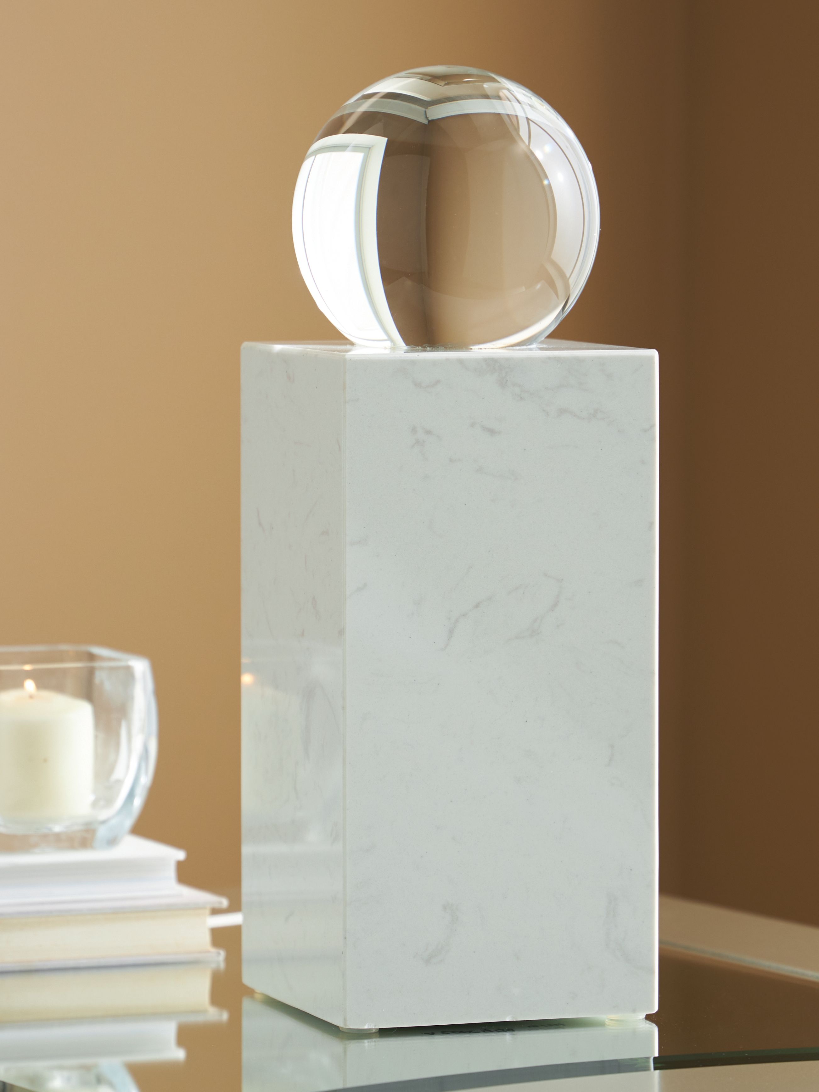 White glass sphere on white marble pedestal, angled view