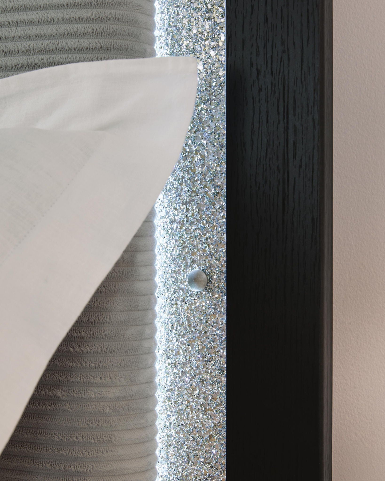Upholstered headboard corner with glittery inset panel and round silver button detail.