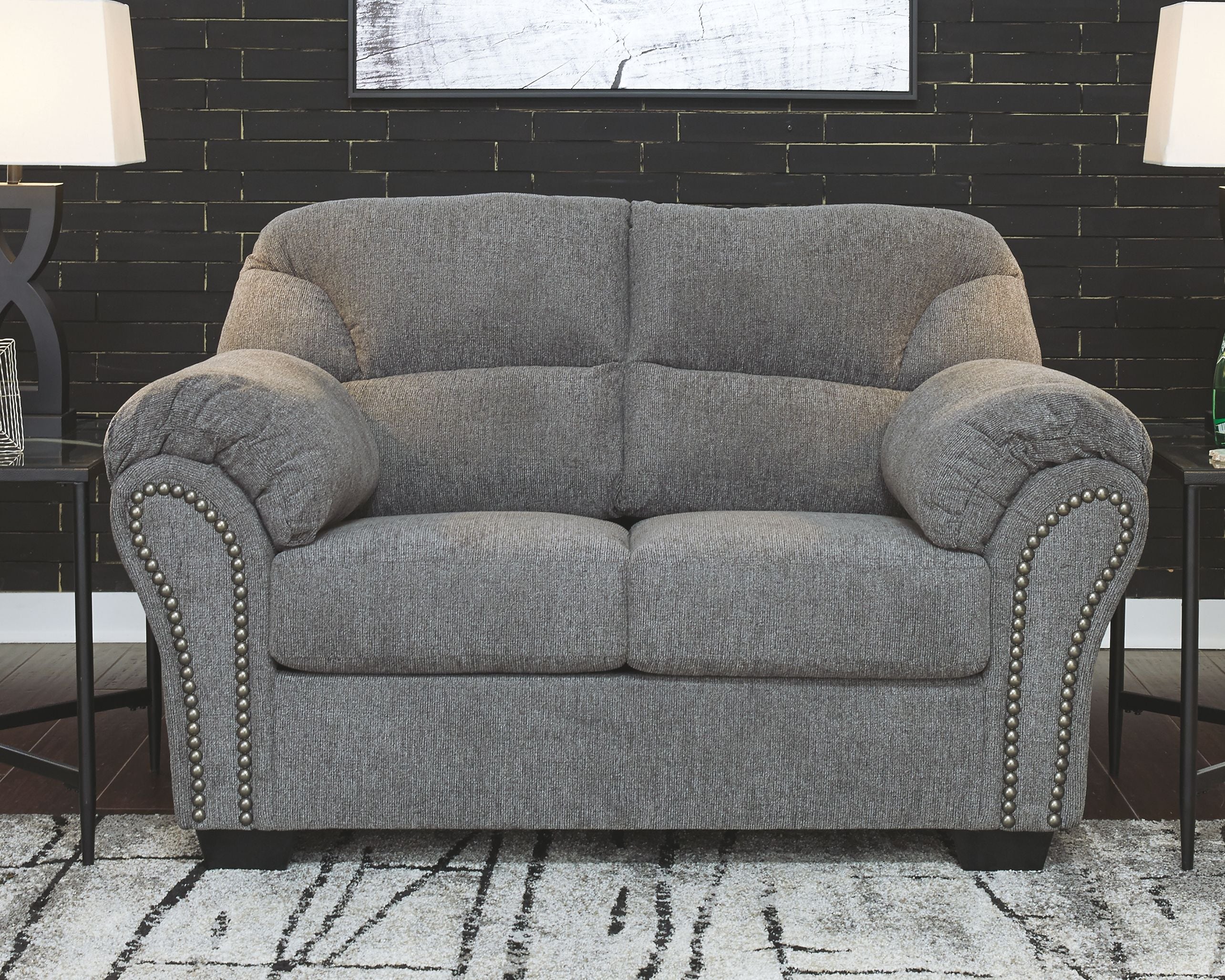 Dark gray loveseat with plush cushions, rolled arms, and studded trim along the edges