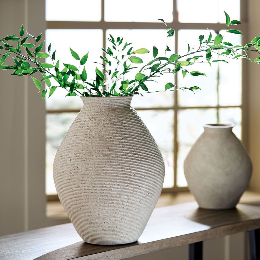 Beige ceramic vase with textured surface and greenery arrangement on tabletop