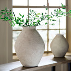 Beige ceramic vase with textured surface and greenery arrangement on tabletop