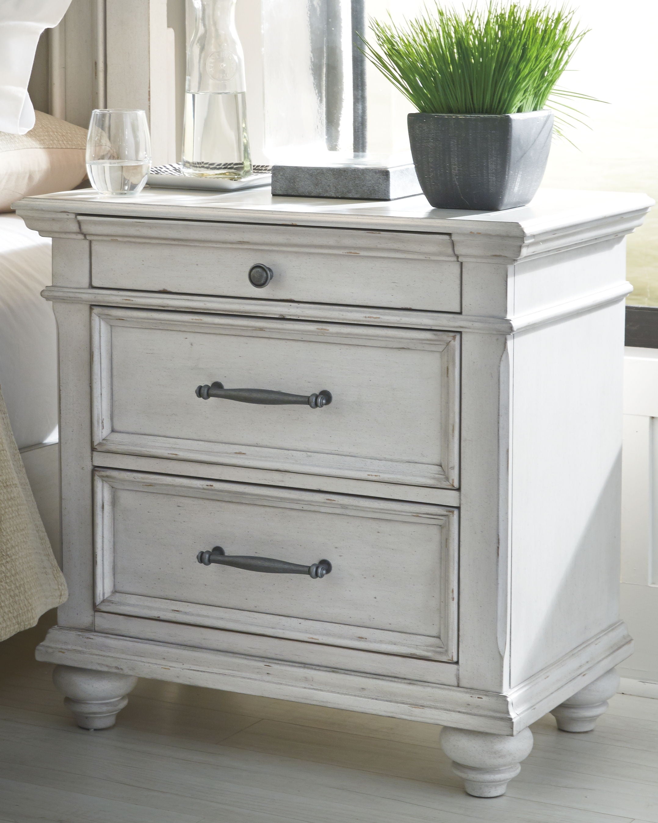 White nightstand with two drawers and curved metal pulls on turned feet