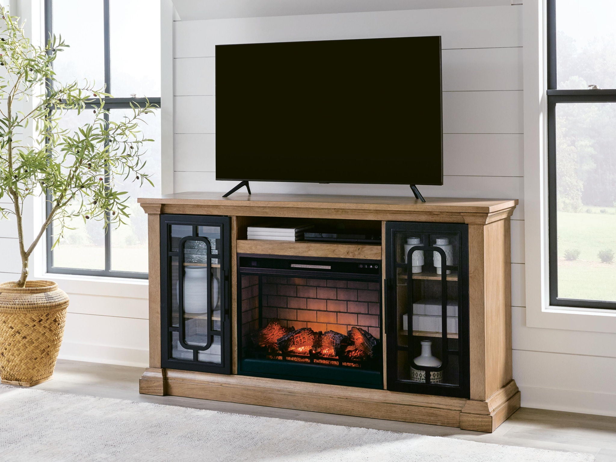 Light brown TV stand with mounted TV, glass doors, and electric fireplace insert beneath.