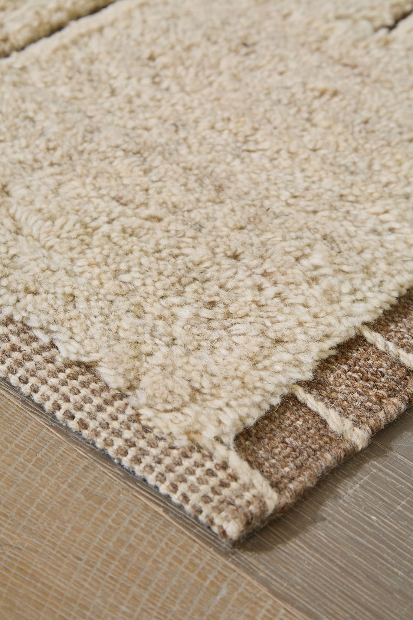 Beige rug corner with textured short pile and woven border