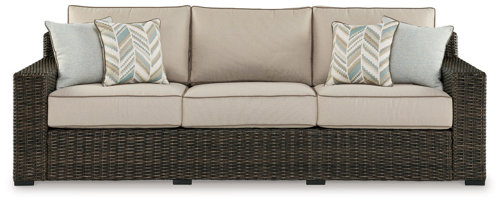 Brown wicker sofa with three beige cushions and two patterned accent pillows